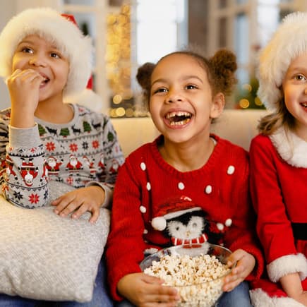 Drei weihnachtliche gekleidete Mädchen vor dem Fernseher.