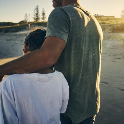 Vater legt den Arm um seinen Sohn am Strand.