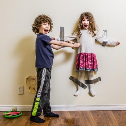 Junge klebt seine kleine Schwester im Spiel an der Wand fest.
