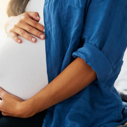 Schwangere Frau hält ihren Babybauch in den Händen. 
