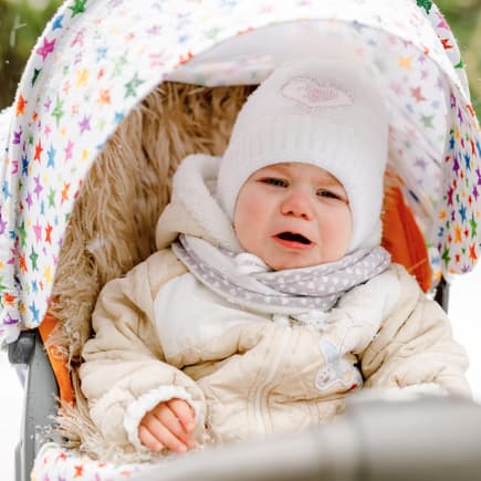 Ein Kleinkind ohne Handschuhe weint im Buggy im Winter.