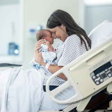 Mama hält ihr Neugeborenes glücklich im Arm.