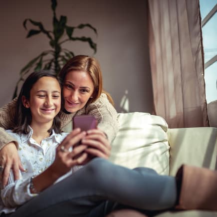Mutter und Tochter mit Smartphone auf dem Sofa: Elektronikartikel für Kinder kann man auch gebraucht kaufen