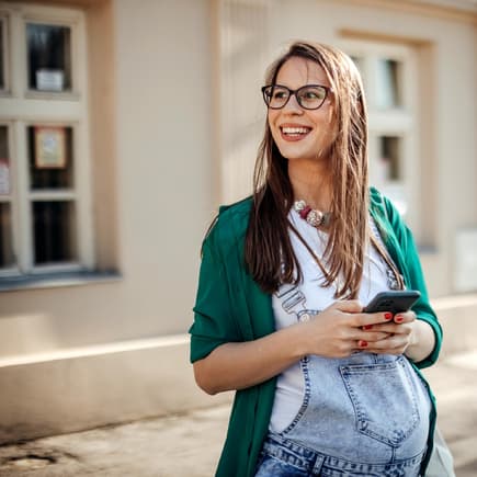 Frau in der Schwangerschaft mit einem Handy in der Hand: Eine Schwangerschafts-App kann helfen. 
