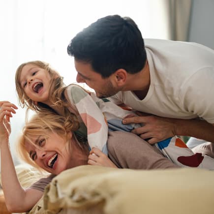 Eltern und Kind liegen im Familienbett und lachen.