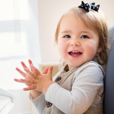 Baby-Mädchen sitzt am Klavier, klatscht und lacht vergnügt.