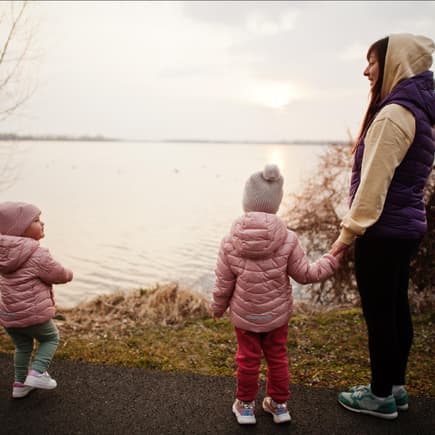 Mutter steht mit zwei kleinen Mädchen am See.