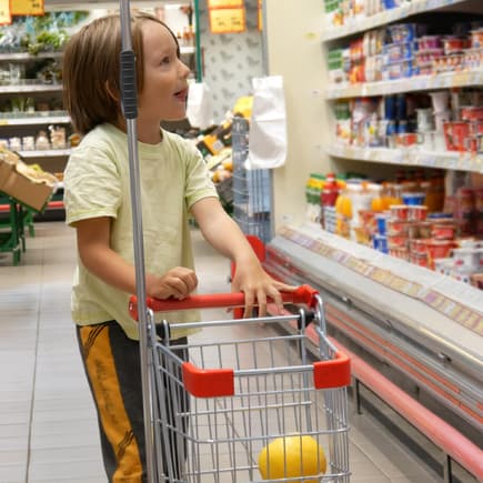 Ein Junge im Supermarkt mit kleinem Einkaufswagen