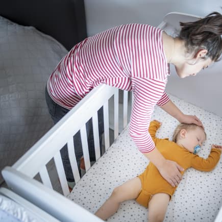 Mutter legt ihr schlafendes Baby ins Bett.