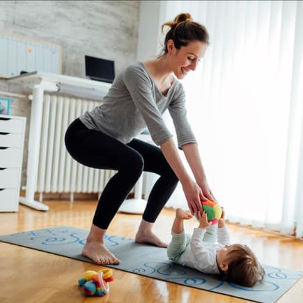 Eine Mutter trainiert ihren Beckenboden, während ihr Baby vor ihr liegt.