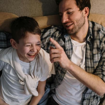 Ein Vater tickt seinen Sohn mit dem Finger an, der bereits zu lachen anfängt.