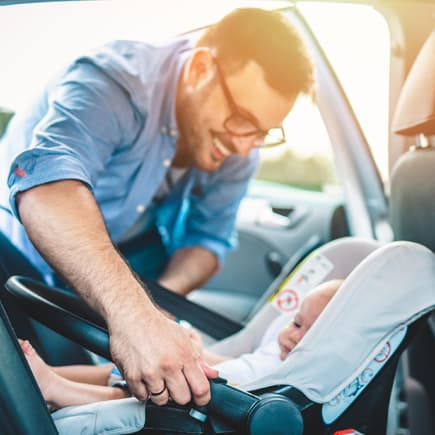 Vater schnallt sein Baby im Auto an.