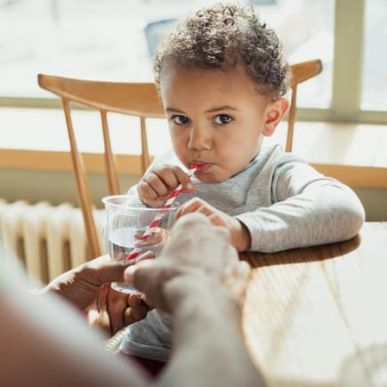 Kleiner Junge trinkt Wasser durch einen Papierstrohhalm.