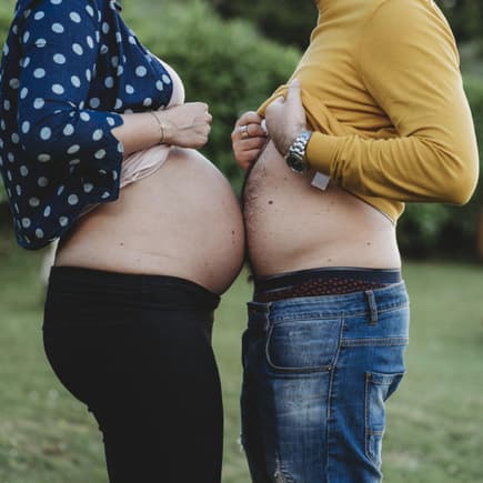 Schwangere Frau und ihr Mann halten ihre Bäuche aneinander.