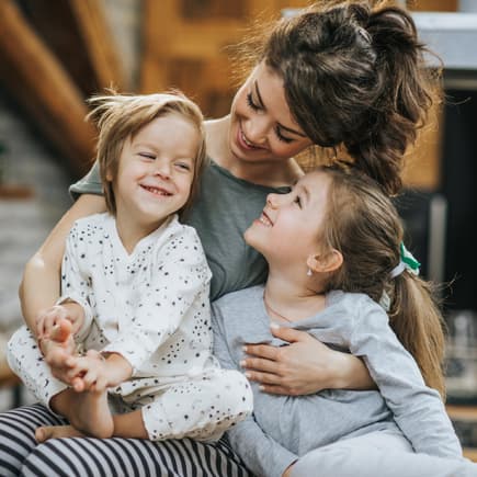 Mama hält ihre zwei Kindern im Arm.