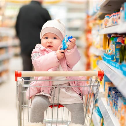 Ein kleines Baby hat in einem Supermarkt einen Quetschie in der Hand. 