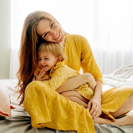 Mama und Kind umarmen sich auf dem Bett.