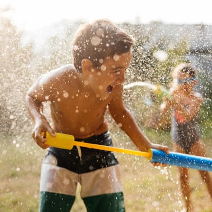 Junge spielt im Garten mit Wasserpistole.