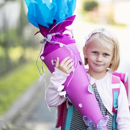 Ein kleines Mädchen hält eine Schultüte in der Hand. 