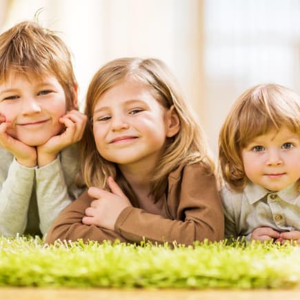 Drei Kinder liegen auf dem Teppich.