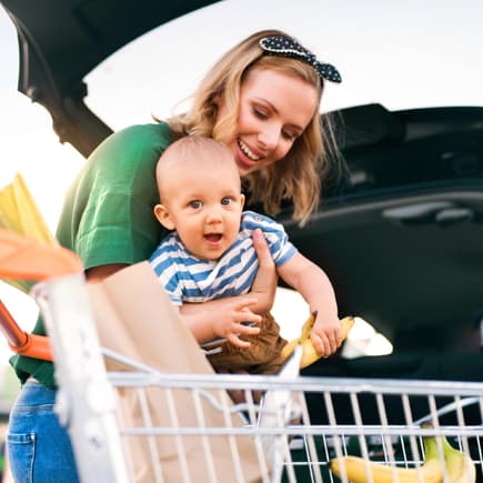 Mutter mit Baby und Einkaufswagen am Auto
