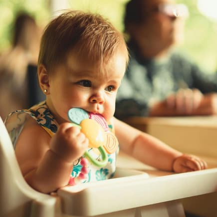 Baby im Hochstuhl kaut auf einem Beißring