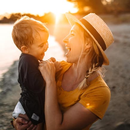 Mutter und Sohn lachend am Strand bei Sonnenuntergang.