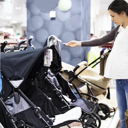 Eine Mutter mit Babybauch steht im Geschäft und schaut sich Kinderwagen an. 