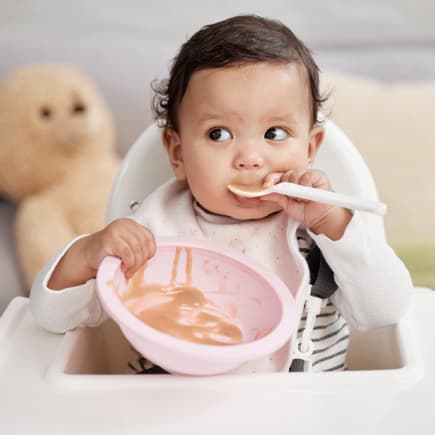 Baby löffelt Obstbrei.