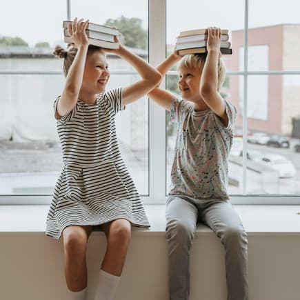 Fröhliche Kinder mit Büchern auf dem Kopf.