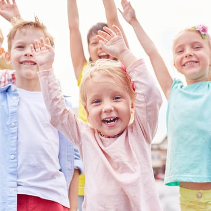 Lachende Kinder mit erhobenen Armen.