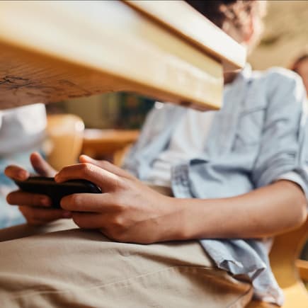 Junge spielt unter dem Schultisch am Smartphone.