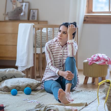 Erschöpfte Frau sitzt auf dem Boden im Kinderzimmer.
