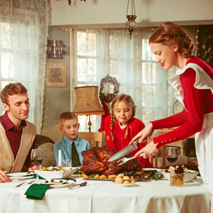 Frau im roten Kleid serviert ihrer Familie einen Braten.