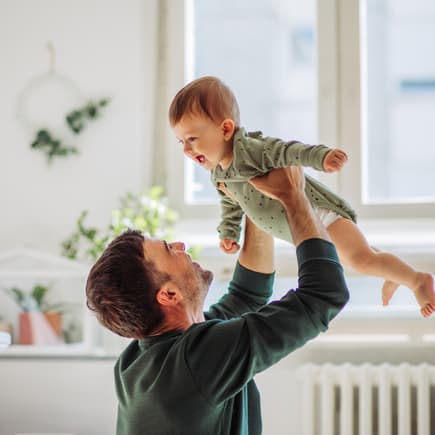 Papa hebt lachendes Baby in die Luft.