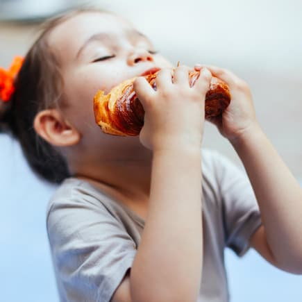 Ein Mädchen beißt in ein Croissant.