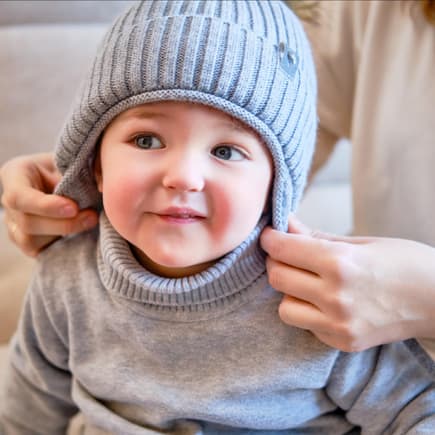 Kleinkind bekommt von der Mutter eine Mütze aufgesetzt.