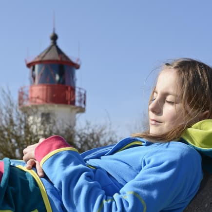 Mädchen chillt vor einem Leuchtturm. 