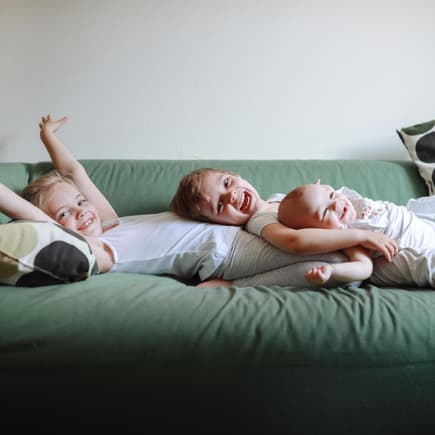 Drei lachende Geschwister liegen auf dem Sofa.