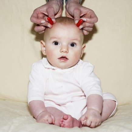 Baby bekommt rote Hörner an die Stirn gehalten.