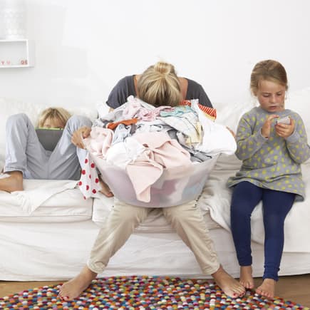 Erschöpfte Mutter Wäschekorb auf dem Schoß auf dem Sofa.