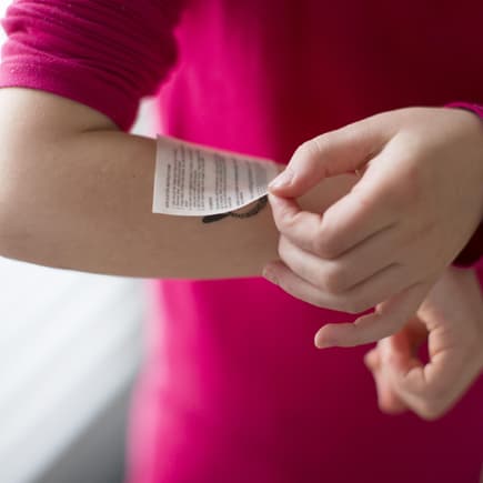 Kind klebt sich ein Tattoo auf den Arm.