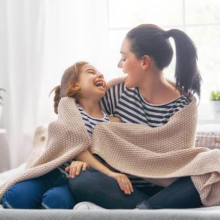  Mutter und Tochter sitzen lachend auf dem Sofa.