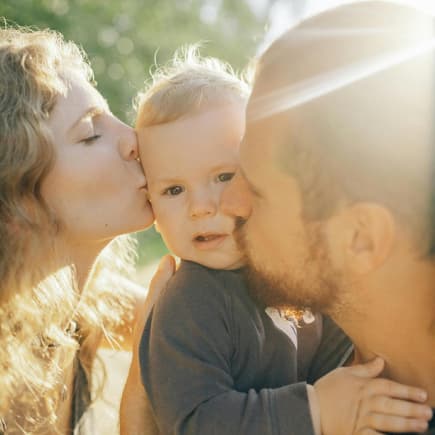 Eltern küssen ihr Baby in der Sonne. 