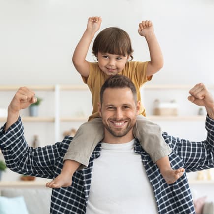 Vater trägt Sohn auf den Schultern, beide zeigen den Bizeps.