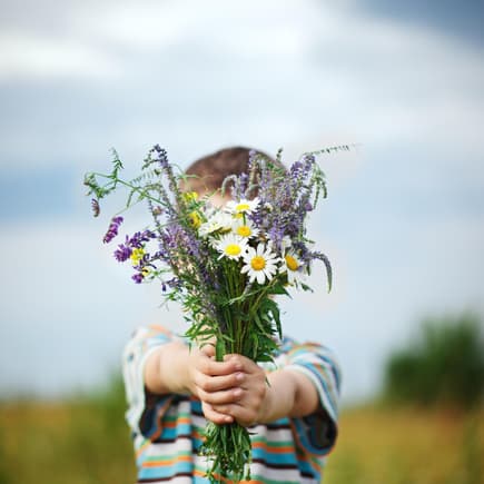 Junge hält Blumenstrauß in die Kamera.