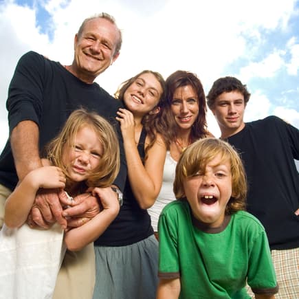 Patchworkfamilie mit vier Kindern vor blau-wolkigem Himmel.