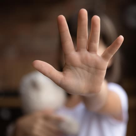 Kind mit Kuscheltier in der einen Hand streckt andere Hand in Stopp-Geste nach vorne.