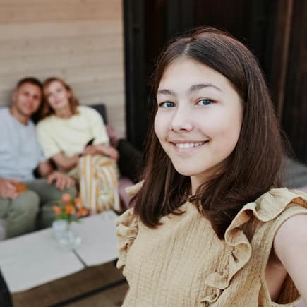 Jugendliche macht Selfie mit sich und ihren Eltern im Hintergrund.