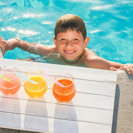 Junge im Pool vor drei Gläsern Saft.